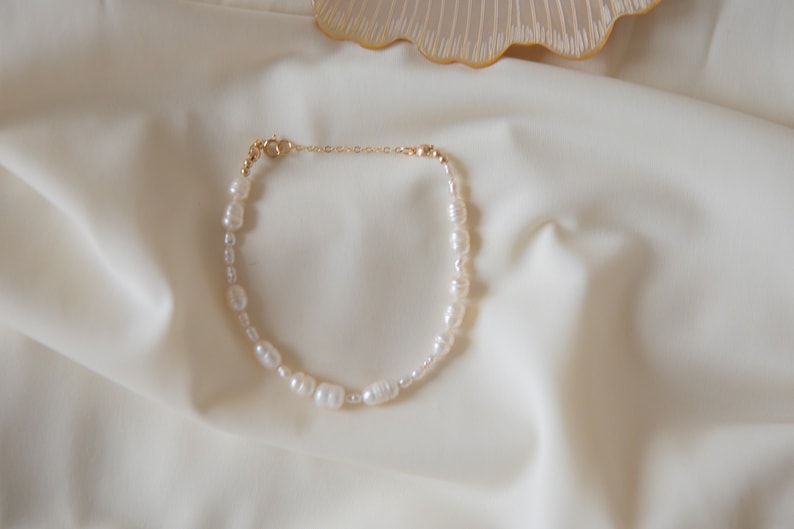 May include: A delicate pearl necklace with a gold clasp. The necklace is made of small, white pearls and is strung on a thin gold chain.