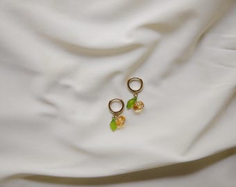May include: A pair of gold hoop earrings with small, dangling charms. Each charm features a yellow and orange glass bead that resembles a flower, with a green leaf attached.