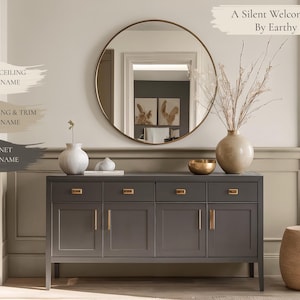 May include: A dark gray cabinet with gold hardware is the focal point of this interior design. A large round mirror hangs above the cabinet, reflecting the room. The text "A Silent Welcome Formed By Earthy Hues" is displayed at the top of the image.
