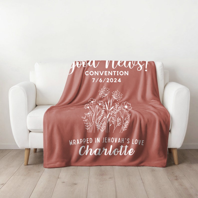 May include: A red fleece blanket with white text and a floral design. The text reads "good news! Convention 7/6/2024 Wrapped in Jehovah's love Charlotte"