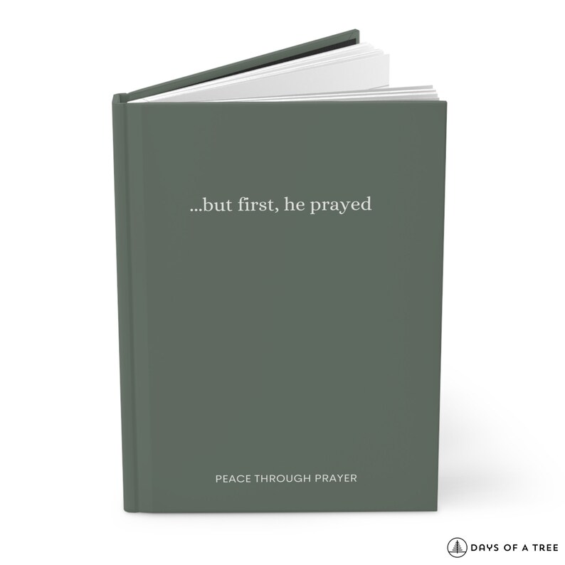 Peut inclure: Un journal &agrave; couverture rigide vert avec le texte "...but first, he prayed" et "PEACE THROUGH PRAYER" sur la couverture. Le journal est ferm&eacute; et les pages sont l&eacute;g&egrave;rement ouvertes.