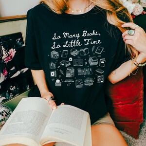 May include: A black t-shirt with a white graphic that says "So Many Books, So Little Time". The graphic features a variety of book illustrations, including stacks of books, open books, and books with bookmarks.