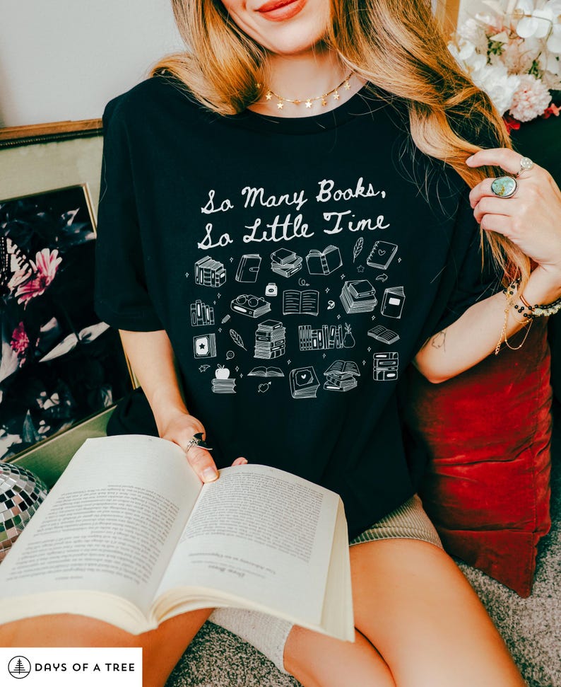 May include: A black t-shirt with a white graphic that says "So Many Books, So Little Time". The graphic features a variety of book illustrations, including stacks of books, open books, and books with bookmarks.