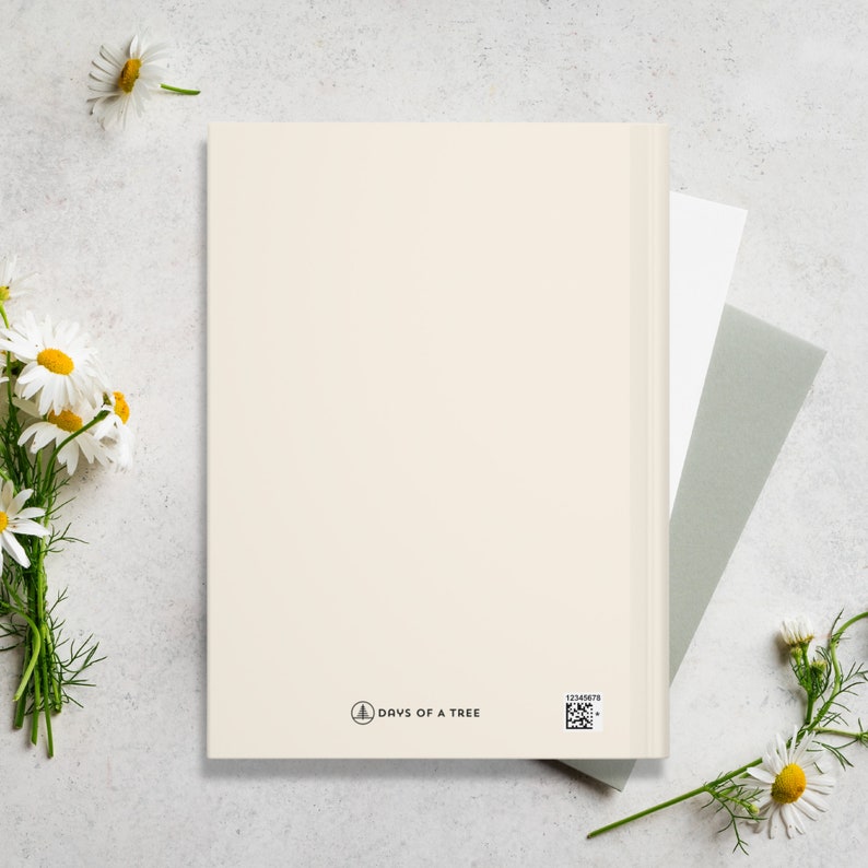 May include: A blank, cream-colored journal with a white spine and a small logo that says "Days of a Tree" on the bottom right corner. The journal is on a white surface with white daisies.