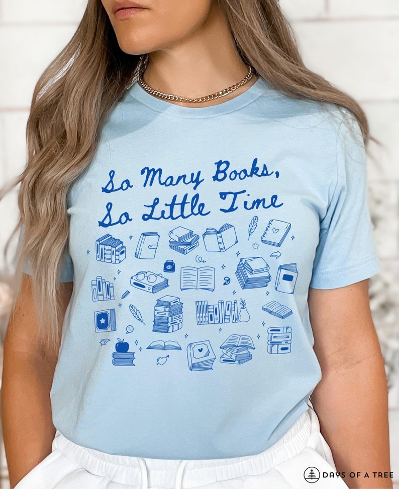 May include: A light blue t-shirt with the text "So Many Books, So Little Time" in blue lettering. The shirt is decorated with a variety of blue illustrations of books, glasses, feathers, and other book-related items.