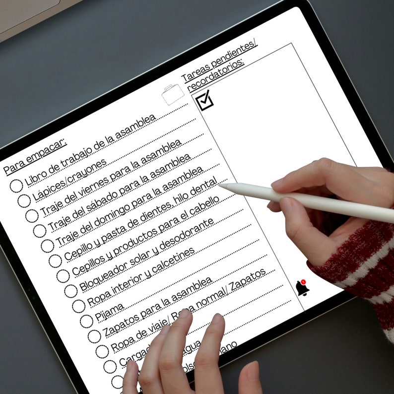 May include: A checklist on a tablet screen with a white stylus. The checklist is titled "Para empacar" and includes items such as "Libro de trabajo de la asamblea", "L&aacute;pices/crayones", and "Traje del viernes para la asamblea".