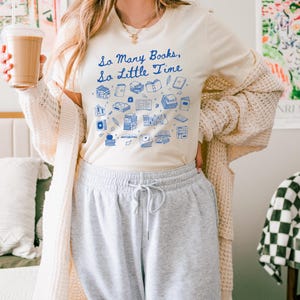 May include: A white t-shirt with a blue graphic of books and the text "So Many Books, So Little Time".