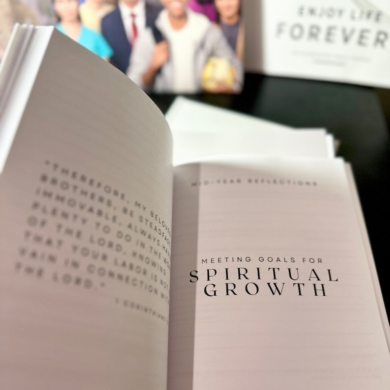 May include: An open book with the text "Meeting Goals for Spiritual Growth" in large, bold letters. The book's pages are white, and the background includes a blurred image and the words "Enjoy Life Forever."