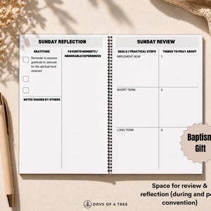 May include: Open spiral-bound notebook with sections for Sunday reflection and review. The notebook includes prompts for gratitude, goals, and prayer. A beige pen rests on the left. The text "Baptism Gift" is visible.