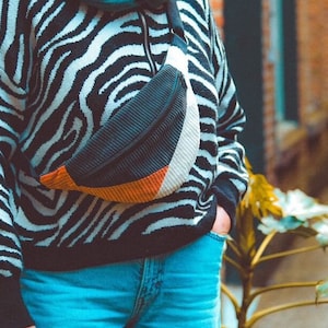 Peut inclure: Une personne portant un pull à rayures noires et blanches en motif zèbre avec une écharpe turquoise et une banane noire, blanche et orange.