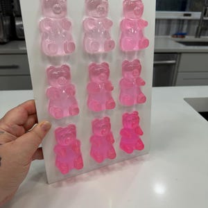 Pu&ograve; includere: Uno stampo rettangolare bianco riempito con dodici caramelle gommose a forma di orsetto rosa. Gli orsetti gommosi sono disposti in tre file da quattro, con diverse tonalit&agrave; di rosa. Lo stampo &egrave; tenuto contro una superficie bianca.