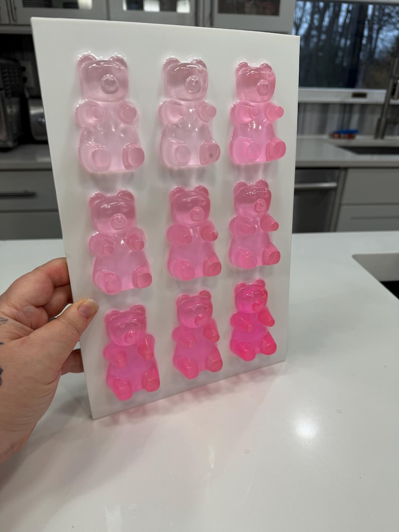 Pu&ograve; includere: Uno stampo rettangolare bianco riempito con dodici caramelle gommose a forma di orsetto rosa. Gli orsetti gommosi sono disposti in tre file da quattro, con diverse tonalit&agrave; di rosa. Lo stampo &egrave; tenuto contro una superficie bianca.