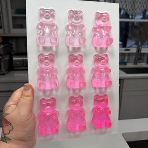 Pu&ograve; includere: Uno stampo rettangolare trasparente riempito con nove caramelle gommose a forma di orsetto rosa. Gli orsetti gommosi sono disposti in tre file da tre, ognuno con una forma di orsetto distinta. Lo stampo &egrave; tenuto su uno sfondo neutro.