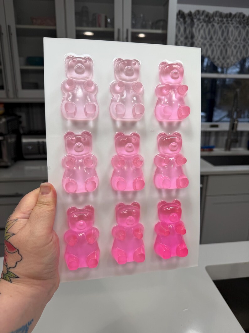 Pu&ograve; includere: Uno stampo rettangolare trasparente riempito con nove caramelle gommose a forma di orsetto rosa. Gli orsetti gommosi sono disposti in tre file da tre, ognuno con una forma di orsetto distinta. Lo stampo &egrave; tenuto su uno sfondo neutro.