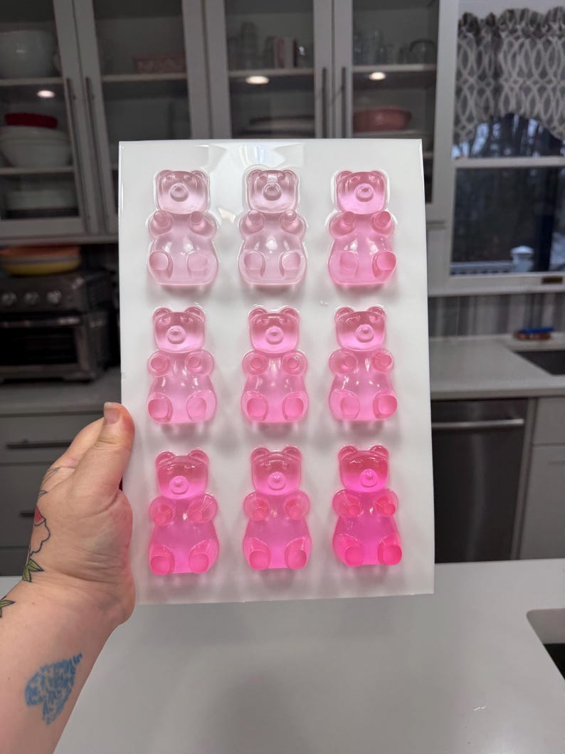 Pu&ograve; includere: Uno stampo rettangolare trasparente riempito con dodici orsetti gommosi rosa. Gli orsetti gommosi sono disposti in tre file da quattro. Lo stampo &egrave; tenuto davanti a uno sfondo di cucina.