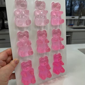 Pu&ograve; includere: Un vassoio bianco contiene nove caramelle gommose a forma di orsetto, in varie tonalit&agrave; di rosa. Gli orsetti gommosi sono disposti in tre file da tre, con l'intensit&agrave; del colore che aumenta dall'alto verso il basso. Gli orsetti sono traslucidi.