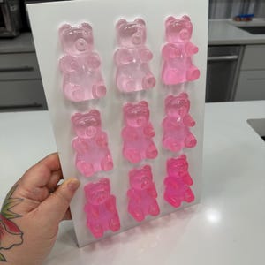 Pu&ograve; includere: Uno stampo rettangolare bianco pieno di nove caramelle gommose a forma di orsetto rosa. Gli orsetti gommosi sono disposti in tre file da tre, con diverse tonalit&agrave; di rosa. Le caramelle sono traslucide e sembrano appena fatte.
