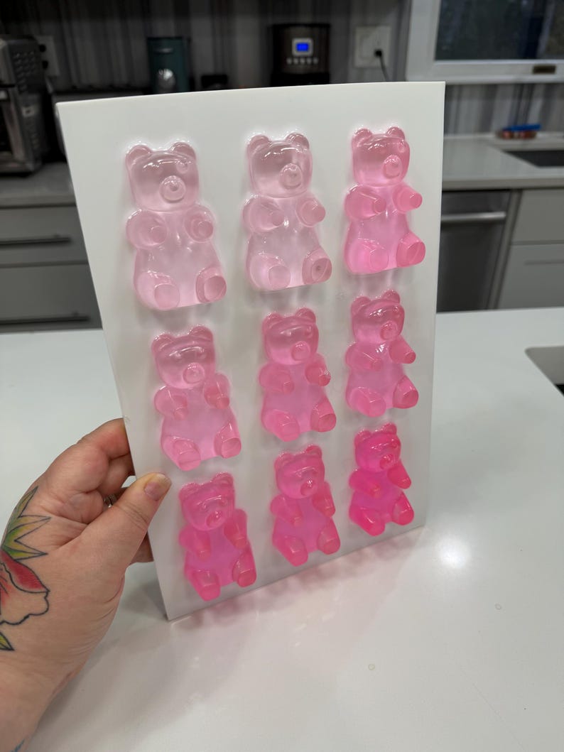 Pu&ograve; includere: Uno stampo rettangolare bianco pieno di nove caramelle gommose a forma di orsetto rosa. Gli orsetti gommosi sono disposti in tre file da tre, con diverse tonalit&agrave; di rosa. Le caramelle sono traslucide e sembrano appena fatte.