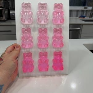 Pu&ograve; includere: Un vassoio rettangolare bianco con dodici caramelle gommose a forma di orsetto rosa. Gli orsetti gommosi sono disposti in tre file da quattro. Le caramelle sono di colore rosa traslucido e il vassoio &egrave; tenuto da una mano.