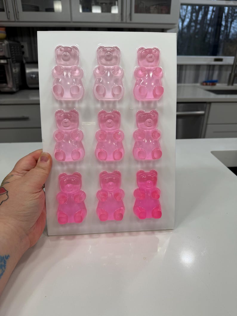 Pu&ograve; includere: Un vassoio rettangolare bianco con dodici caramelle gommose a forma di orsetto rosa. Gli orsetti gommosi sono disposti in tre file da quattro. Le caramelle sono di colore rosa traslucido e il vassoio &egrave; tenuto da una mano.