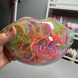 May include: A clear glass vase filled with colorful, tangled string. The string is pink, orange, green, and purple.