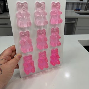 Pu&ograve; includere: Uno stampo bianco pieno di nove caramelle gommose a forma di orsetto rosa. Gli orsetti gommosi sono disposti in tre file da tre, con diverse sfumature di rosa. Lo stampo &egrave; tenuto in mano e lo sfondo &egrave; una cucina.