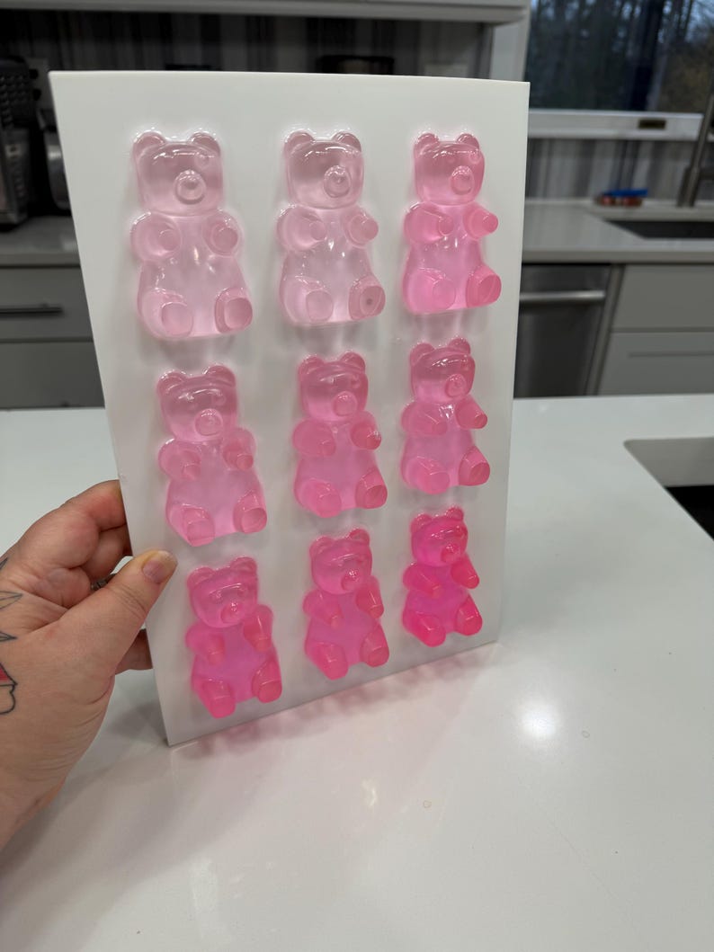 Pu&ograve; includere: Uno stampo bianco pieno di nove caramelle gommose a forma di orsetto rosa. Gli orsetti gommosi sono disposti in tre file da tre, con diverse sfumature di rosa. Lo stampo &egrave; tenuto in mano e lo sfondo &egrave; una cucina.