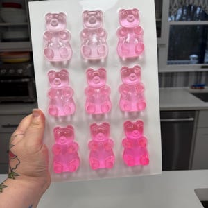 Pu&ograve; includere: Uno stampo di plastica bianca pieno di nove caramelle gommose a forma di orsetto in varie tonalit&agrave; di rosa. Gli orsetti gommosi sono disposti in tre file da tre. Le caramelle sono traslucide e sembrano appena fatte.