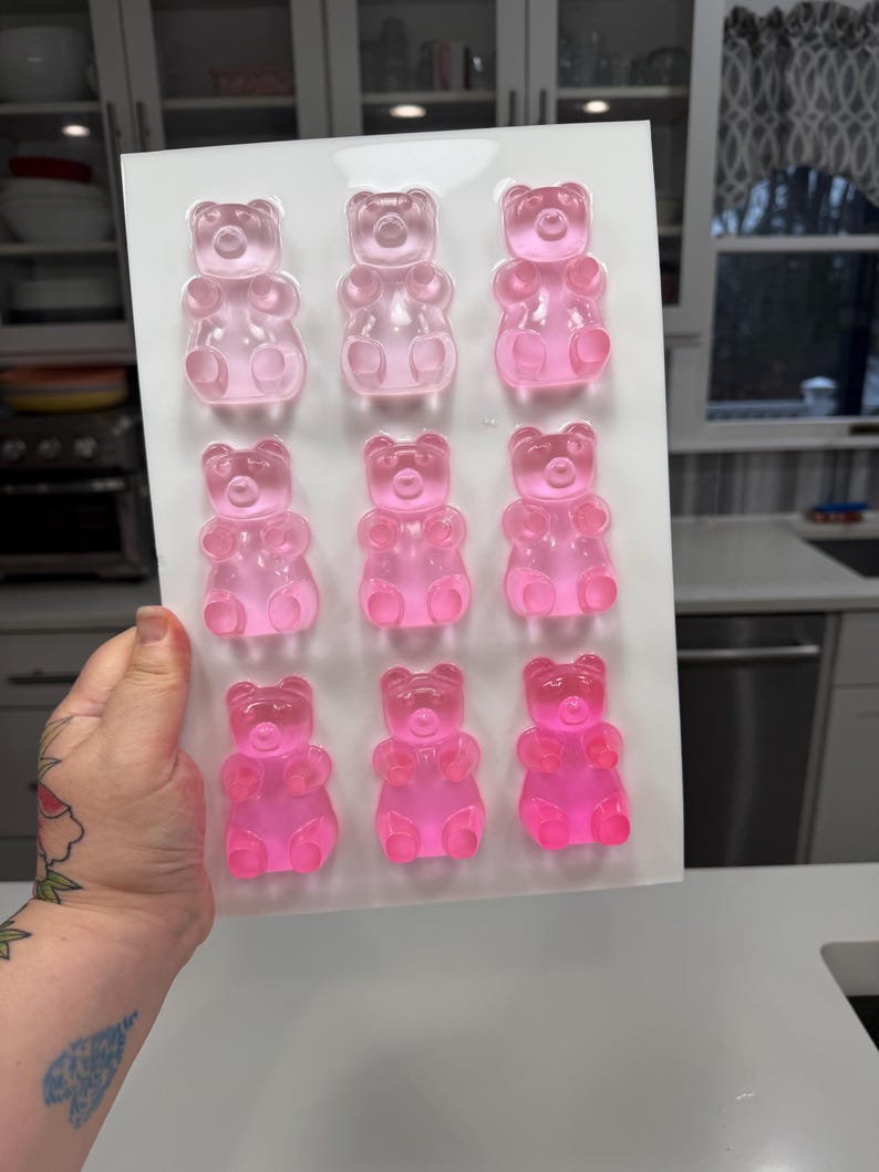 Pu&ograve; includere: Uno stampo di plastica bianca pieno di nove caramelle gommose a forma di orsetto in varie tonalit&agrave; di rosa. Gli orsetti gommosi sono disposti in tre file da tre. Le caramelle sono traslucide e sembrano appena fatte.