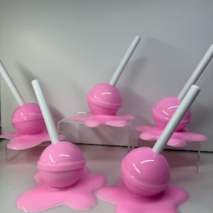 Op de afbeelding: Roze lolly's met witte stokjes, die lijken te smelten op een bijpassende roze basis. De lolly's zijn geplaatst op heldere, verhoogde platforms. De afbeelding toont een speels, snoep-thema ontwerp.
