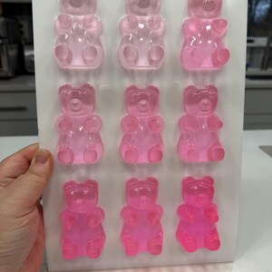 Pu&ograve; includere: Un vassoio di nove caramelle gommose a forma di orsetto rosa in varie tonalit&agrave; di rosa. Gli orsetti gommosi sono disposti in tre file da tre, con un aspetto chiaro e traslucido. Il vassoio &egrave; tenuto da una mano.