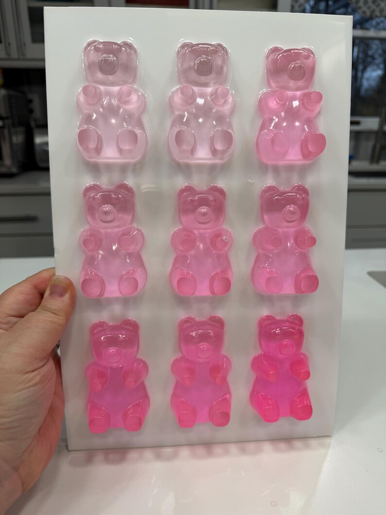 Pu&ograve; includere: Un vassoio di nove caramelle gommose a forma di orsetto rosa in varie tonalit&agrave; di rosa. Gli orsetti gommosi sono disposti in tre file da tre, con un aspetto chiaro e traslucido. Il vassoio &egrave; tenuto da una mano.