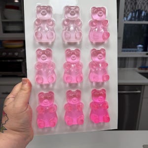 Pu&ograve; includere: Uno stampo di plastica trasparente riempito con nove caramelle gommose a forma di orsetto rosa. Gli orsetti gommosi sono disposti in tre file da tre. Lo stampo &egrave; tenuto da una mano, con una cucina sullo sfondo.