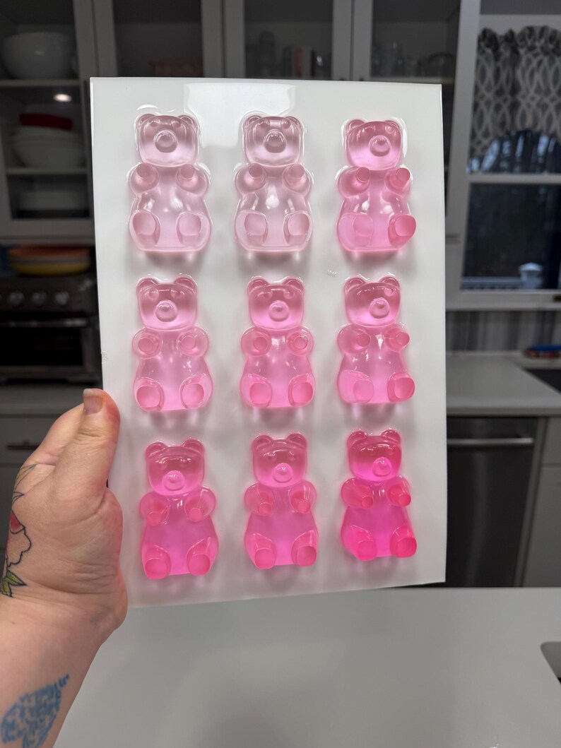 Pu&ograve; includere: Uno stampo di plastica trasparente riempito con nove caramelle gommose a forma di orsetto rosa. Gli orsetti gommosi sono disposti in tre file da tre. Lo stampo &egrave; tenuto da una mano, con una cucina sullo sfondo.