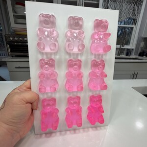 Pu&ograve; includere: Un vassoio rettangolare bianco che contiene dodici caramelle gommose a forma di orsetto rosa. Gli orsetti gommosi sono disposti in tre file da quattro, con diverse tonalit&agrave; di rosa. Lo sfondo mostra una cucina con mobili bianchi e un piano di lavoro.