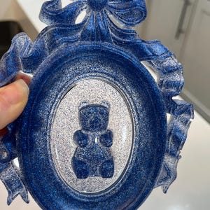 Op de afbeelding: Een blauw glitterhars fotolijst met een witte binnenkant en een blauw glitterbeer silhouet erin. De lijst is versierd met een blauw glitter strikje.