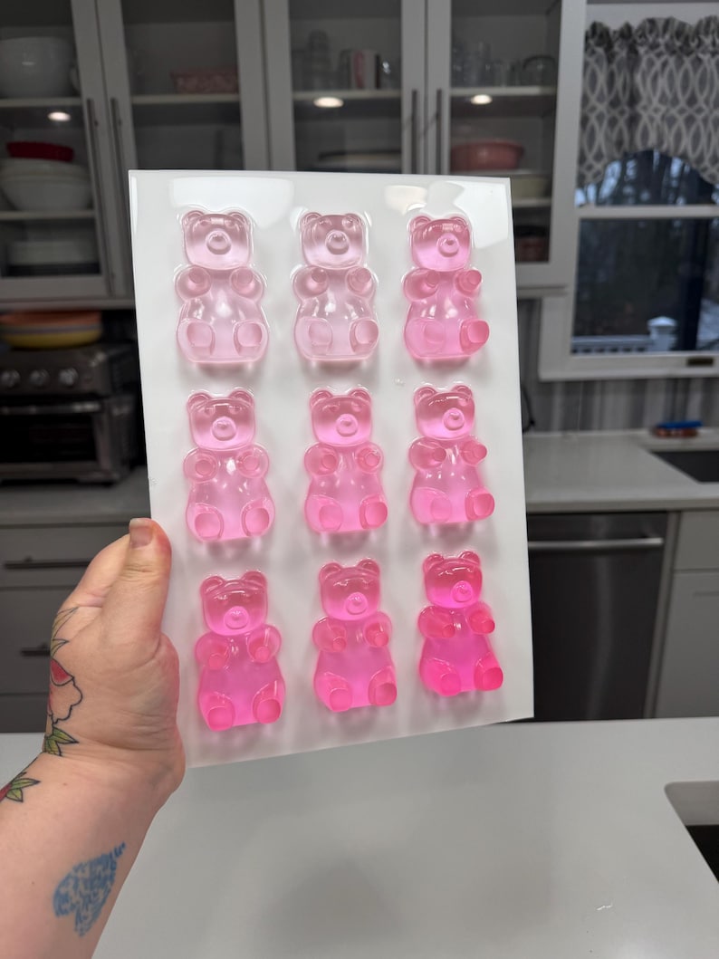 Pu&ograve; includere: Uno stampo di plastica trasparente riempito con dodici caramelle gommose a forma di orsetto rosa. Gli orsetti gommosi sono disposti in tre file da quattro. Le caramelle hanno un aspetto traslucido e sono di una tonalit&agrave; rosa vibrante. Lo stampo &egrave; tenuto su uno sfondo bianco.
