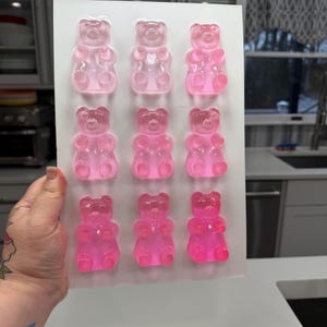 Pu&ograve; includere: Uno stampo rettangolare bianco riempito con dodici caramelle gommose a forma di orsetto in varie tonalit&agrave; di rosa. Gli orsetti gommosi sono disposti in tre file da quattro. Le caramelle sono traslucide e sembrano essere fatte di gelatina.