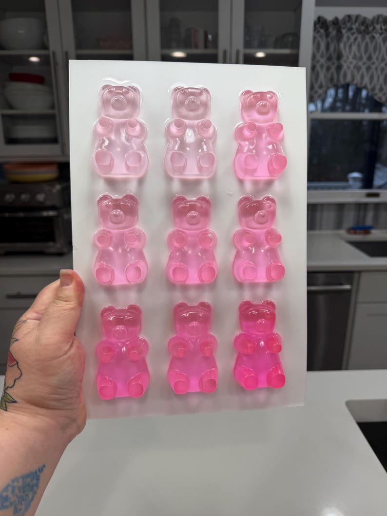 Pu&ograve; includere: Uno stampo di plastica trasparente riempito con nove caramelle gommose a forma di orsetto, in varie tonalit&agrave; di rosa. Gli orsetti gommosi sono disposti in tre file da tre. Lo stampo &egrave; tenuto da una persona.