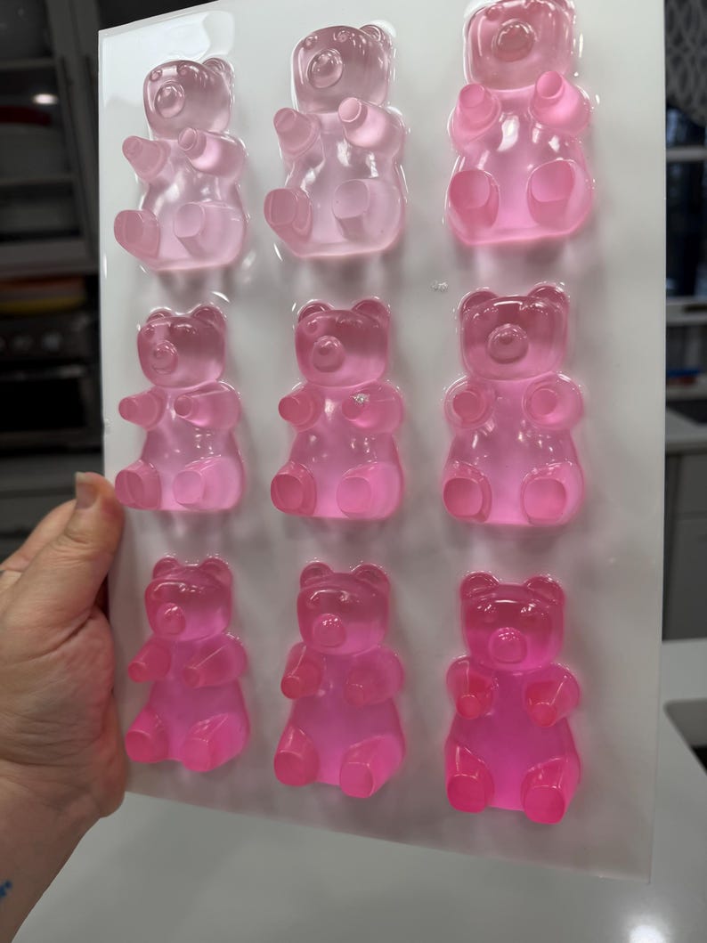Pu&ograve; includere: Uno stampo di plastica trasparente riempito con nove caramelle gommose a forma di orsetto in varie tonalit&agrave; di rosa. Gli orsetti gommosi sono disposti in tre file da tre, con ogni orsetto che mostra dettagli come le zampe e una faccia sorridente. Lo stampo &egrave; tenuto da una mano.