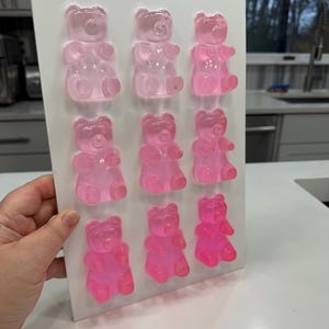 Pu&ograve; includere: Un vassoio rettangolare bianco con nove caramelle gommose a forma di orsetto in varie tonalit&agrave; di rosa. Gli orsetti gommosi sono disposti in tre file da tre, con colori che vanno dal rosa chiaro al fucsia vibrante.