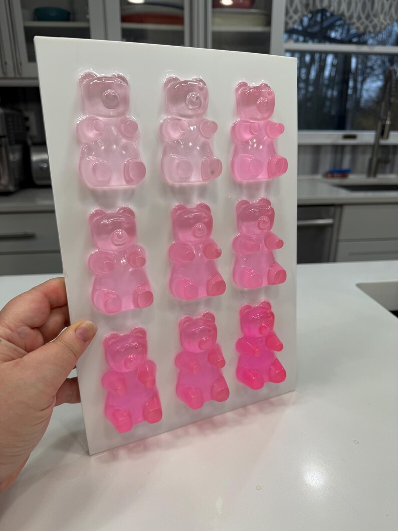 Pu&ograve; includere: Un vassoio rettangolare bianco con nove caramelle gommose a forma di orsetto in varie tonalit&agrave; di rosa. Gli orsetti gommosi sono disposti in tre file da tre, con colori che vanno dal rosa chiaro al fucsia vibrante.