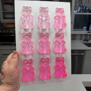 Pu&ograve; includere: Uno stampo di plastica trasparente riempito con dodici caramelle gommose a forma di orsetto rosa. Gli orsetti gommosi sono disposti in tre file da tre, con diverse sfumature di rosa. Lo stampo &egrave; tenuto in mano, con uno sfondo di cucina.