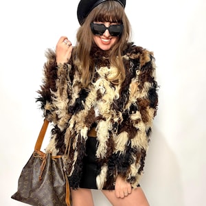 Puede incluir: Una persona con boina negra y gafas de sol, con un abrigo peludo en tonos marrón, negro y crema. También lleva una falda negra y botas negras hasta la rodilla. Se ve un bolso marrón con cierre de cordón.