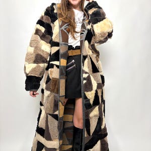 May include: A long patchwork coat in shades of black, brown, and cream. The coat features a geometric pattern and a long, flowing design. The coat is worn with a black skirt and boots. The coat is a statement piece.