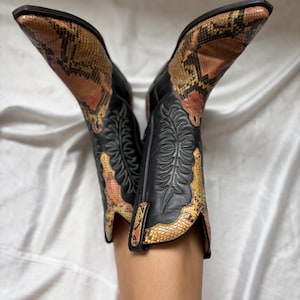 Puede incluir: Botas de vaquero negras con estampado de piel de serpiente en tonos marr&oacute;n, beige y rosa. Las botas tienen puntas puntiagudas y costuras decorativas. Una elecci&oacute;n de calzado elegante.