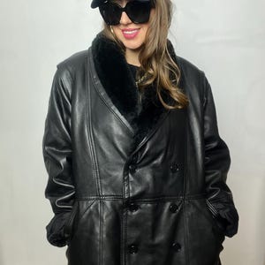 May include: A black leather coat with a faux fur collar and double breasted closure. The coat has a long length and a relaxed fit.