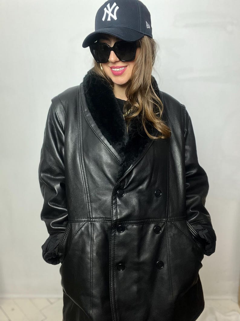 May include: A black leather coat with a faux fur collar and double breasted closure. The coat has a long length and a relaxed fit.