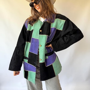 May include: A long-sleeve jacket featuring a patchwork design of black, purple, and mint green suede panels. The jacket has a collared neckline, a front button closure with three gold-toned buttons, and two side pockets.