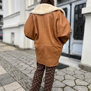 May include: A brown leather jacket with a white shearling collar and brown checkered pants.